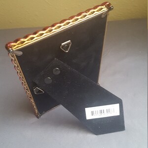 May include: A gold picture frame with a red and gold ornate border. The frame has a black backing with a kickstand and a barcode label that reads "8 1148 02015".