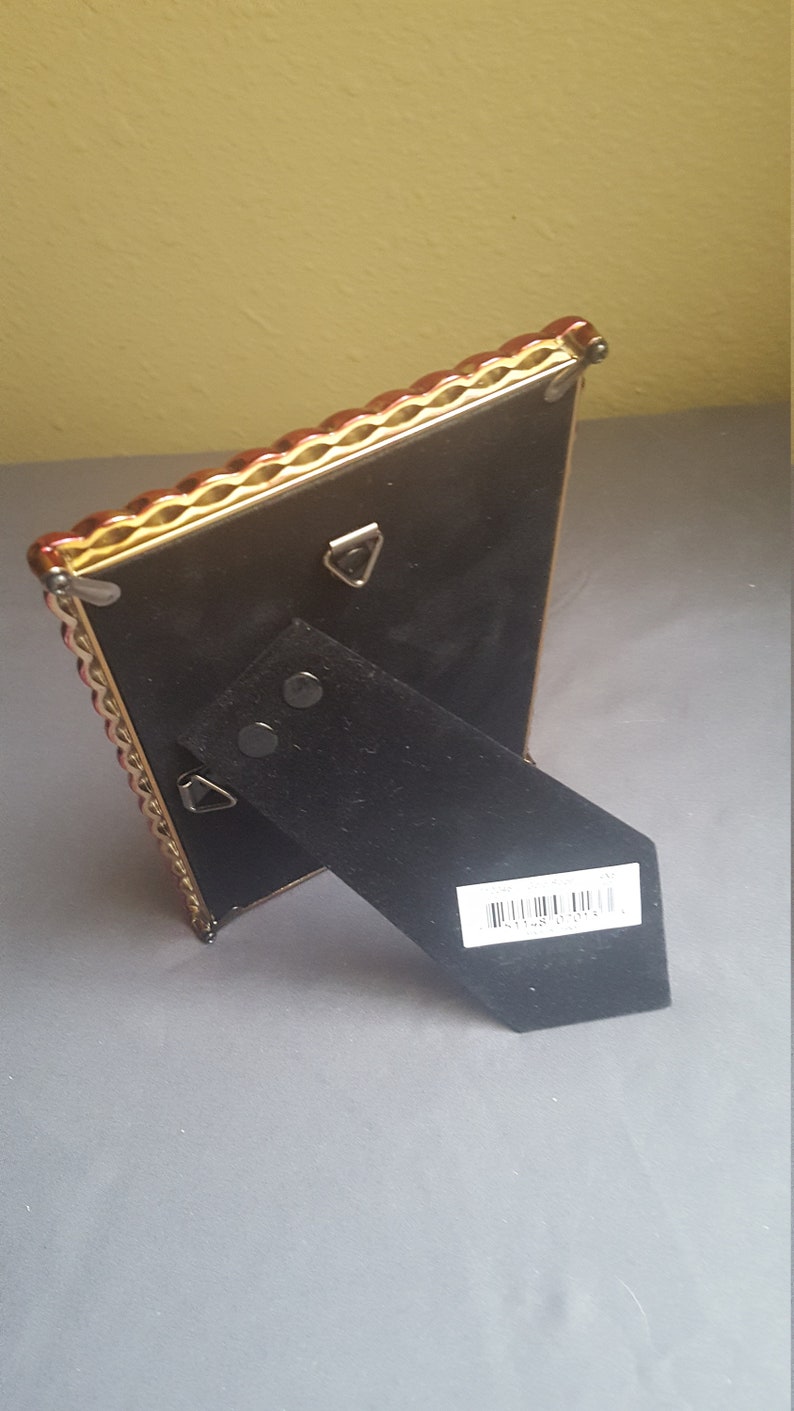 May include: A gold picture frame with a red and gold ornate border. The frame has a black backing with a kickstand and a barcode label that reads "8 1148 02015".
