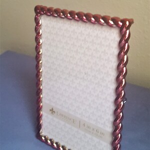 May include: A red and gold picture frame with a braided design. The frame is 4 inches by 6 inches (10 cm x 15 cm).
