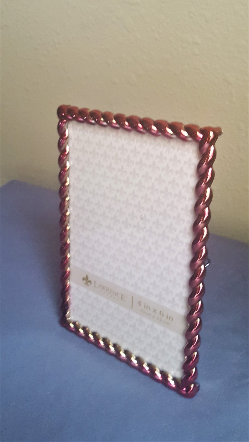 May include: A red and gold picture frame with a braided design. The frame is 4 inches by 6 inches (10 cm x 15 cm).