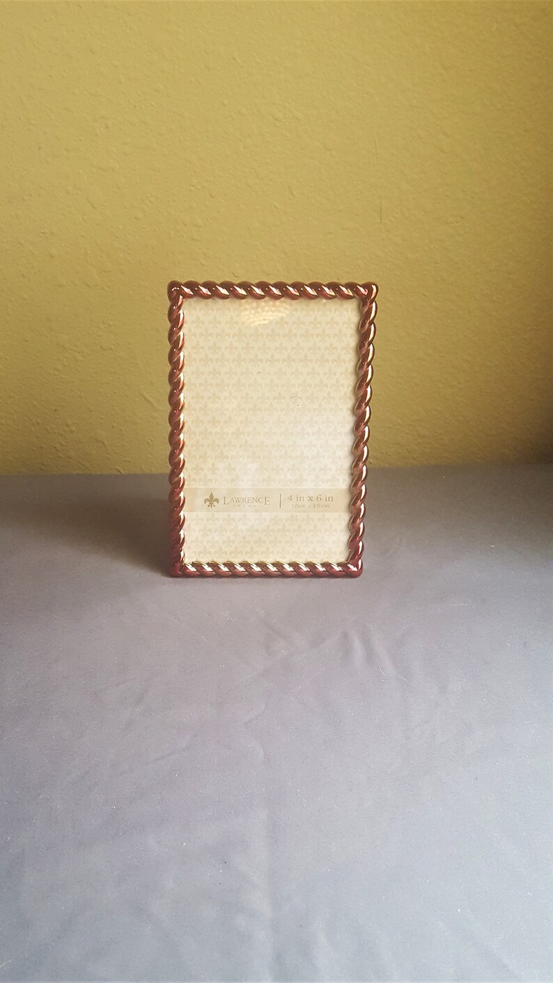May include: A brown picture frame with a rope-like design around the edge. The frame is 4 inches by 6 inches and has a white mat.
