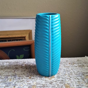 May include: A turquoise blue ceramic vase with a textured, wavy design and a silver stripe down the center.