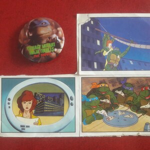 May include: Four Teenage Mutant Ninja Turtles trading cards featuring a scene from the movie. The cards are white with a black border and feature a cartoon image of the turtles. The first card shows the turtles eating pizza. The second card shows the turtles fighting a villain. The third card shows the turtles in a sewer. The fourth card shows the turtles in a city street. The cards also feature the text "Teenage Mutant Ninja Turtles The Movie".