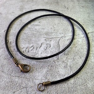 May include: A black leather cord necklace with a bronze spring clasp and a bronze jump ring.
