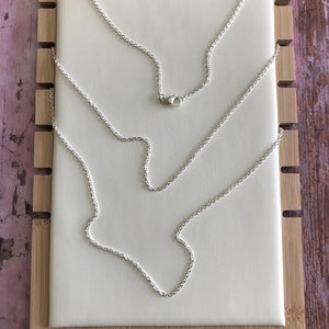 Op de afbeelding: Een zilveren kettingketting op een wit displaybord. De ketting wordt in een lus met de sluiting weergegeven.