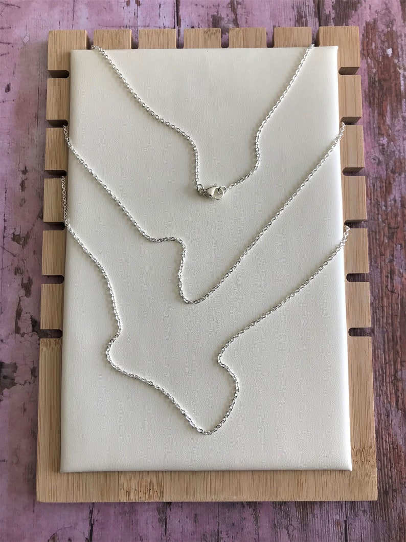 Op de afbeelding: Een zilveren kettingketting op een wit displaybord. De ketting wordt in een lus met de sluiting weergegeven.