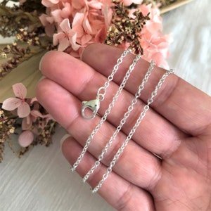 Op de afbeelding: Een zilveren ketting met een karabijn sluiting. De ketting is delicaat en heeft een fijn, kabelachtig ontwerp.