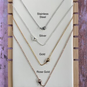 Op de afbeelding: Vier verschillende kettingen die op een houten achtergrond worden getoond. De kettingen zijn van roestvrij staal, zilver, goud en ros&eacute;goud. Elke ketting heeft een sluiting.