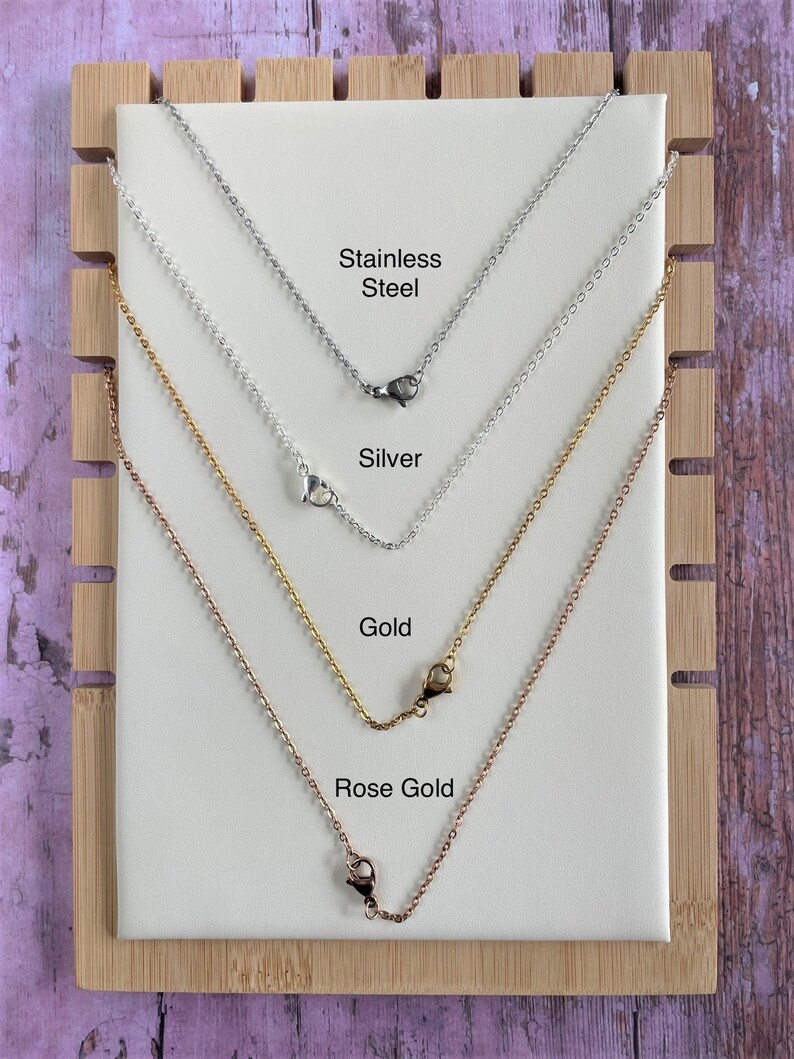Op de afbeelding: Vier verschillende kettingen die op een houten achtergrond worden getoond. De kettingen zijn van roestvrij staal, zilver, goud en ros&eacute;goud. Elke ketting heeft een sluiting.
