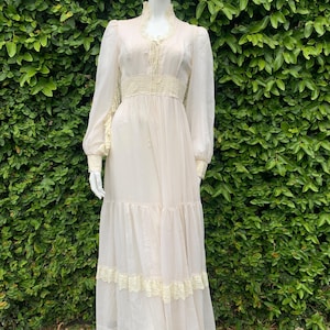 Puede incluir: Un vestido maxi blanco con mangas largas y detalles de encaje. El vestido tiene un corpi&ntilde;o ajustado y una falda fluida con varias capas.