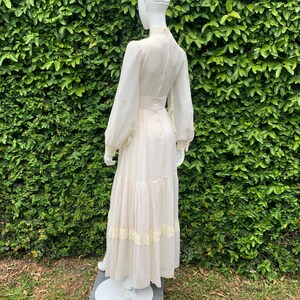 Puede incluir: Un vestido maxi largo blanco con cuello alto y mangas largas. El vestido tiene una falda de capas y ribete de encaje. El vestido est&aacute; hecho de una tela ligera y es perfecto para una boda de verano u otra ocasi&oacute;n especial.
