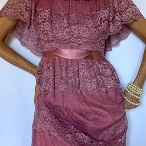 Puede incluir: Un vestido largo de encaje color malva con un escote de volantes y una cinta de raso en la cintura.