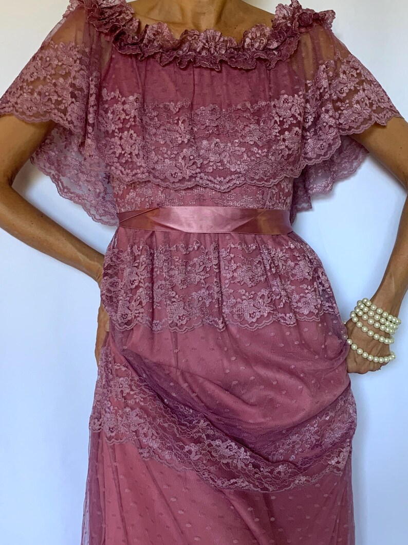 Puede incluir: Un vestido largo de encaje color malva con un escote de volantes y una cinta de raso en la cintura.