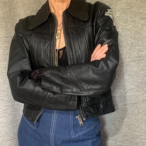 May include: A black leather jacket with a zip fastening and a Harley Davidson logo patch on the left sleeve.