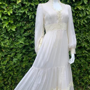 Puede incluir: Un vestido largo blanco de maxi con volantes y detalles de encaje en el escote, la cintura y las mangas. El vestido tiene un corpi&ntilde;o ajustado y una falda fluida.