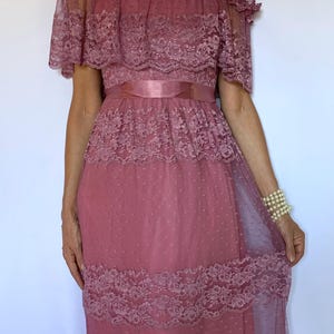 Puede incluir: Un vestido largo de color rosa, de hombros descubiertos, con detalles de encaje y una cinta de raso en la cintura.