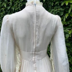 Puede incluir: Un vestido vintage blanco con mangas largas y un ribete de encaje. El vestido tiene un corpi&ntilde;o ajustado y una falda fluida.