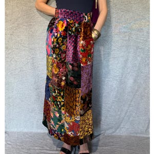 May include: A long, patchwork skirt made of velvet. The skirt is a mix of floral and geometric patterns in shades of pink, purple, red, green, brown, and gold.