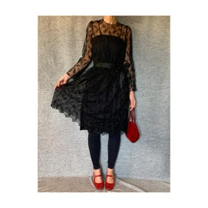 May include: A black sheer dress with a floral pattern and a black ribbon belt. The dress is worn with black leggings and red shoes.
