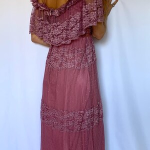 Puede incluir: Un vestido maxi de color rosa polvoriento con hombros descubiertos, una superposici&oacute;n de encaje y una falda de capas.