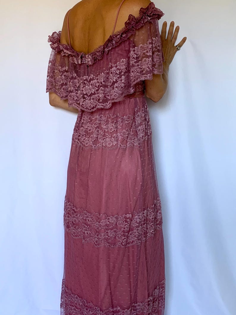 Puede incluir: Un vestido maxi de color rosa polvoriento con hombros descubiertos, una superposici&oacute;n de encaje y una falda de capas.