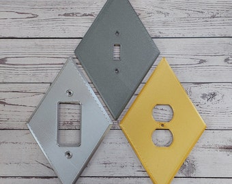 May include: Three diamond-shaped wall plates in gray, silver, and yellow. The gray plate has a light switch, the silver plate has a light switch, and the yellow plate has an electrical outlet.