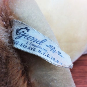 May include: White fabric label with blue text that reads " Gund Mfg. Co. J. Swedlin Inc. 200-5th Ave. N.Y.C. 10, N.Y."