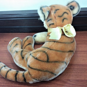 May include: A plush tiger toy with black stripes and a yellow bow. The toy is lying on a wooden surface.
