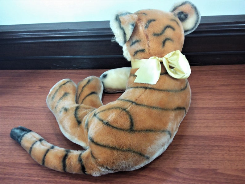 May include: A plush tiger toy with black stripes and a yellow bow. The toy is lying on a wooden surface.