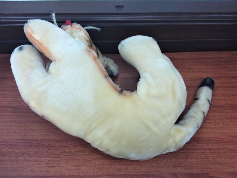 May include: A plush tiger toy with a cream colored body and black and orange stripes. The toy is lying on its back with its legs in the air.