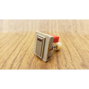 May include: A rectangular beige electrical push button switch featuring a metallic silver center panel with a thin horizontal red indicator line. The component includes a red plastic block, a metal spring, and a small white cylindrical connector.