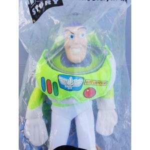 May include: A Buzz Lightyear action figure in a clear plastic bag. The figure is wearing a green and white spacesuit with the words "Buzz Lightyear" on the chest. The figure has a smiling face and purple hair. The bag has the words "Toy Story" printed on it.