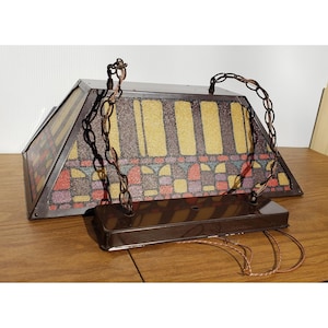 May include: A rectangular hanging light fixture with a brown metal frame and a colorful stained-glass design. The glass features a pattern of yellow, red, purple, and blue geometric shapes. The fixture is suspended by brown metal chains.