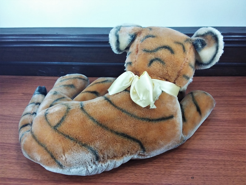 May include: A plush tiger toy with brown and black stripes, lying on its side with its head turned to the right. The tiger has a yellow satin bow tied around its neck.
