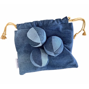 May include: A denim drawstring bag with three denim balls. The bag and balls are various shades of blue. The drawstring is a tan rope. The balls are made of denim fabric and are a fun toy.