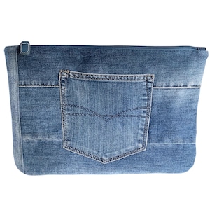 May include: A blue denim pouch with a zipper closure and a pocket on the front. The pouch is made from recycled denim and has a rectangular shape. The pocket is a standard size and shape, with a stitched design.