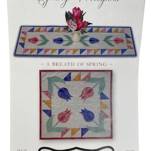 May include: A quilting pattern featuring a table runner and a square quilt block with a floral design. The pattern is called "Spring Whispers" and features a design of tulips in shades of pink, blue, and green. The pattern is from "In the Doghouse Designs" and is identified as IDH20.