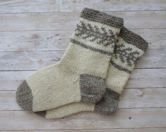 Könnte beinhalten: Ein Paar handgestrickte Socken in Creme, Grau und Taupe. Die Socken haben ein geometrisches Muster in Grau auf dem oberen Teil, mit grauen Fersen, Zehen und Bündchen. Hergestellt aus dickem, warmem Garn, ideal für kaltes Wetter.