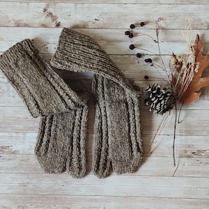 Könnte beinhalten: Ein Paar braune, fingerlose Handschuhe im Zopfstrickmuster mit geteiltem Zehenbereich. Die Handschuhe weisen ein strukturiertes Rippenmuster auf, das sich vom Handgelenk bis zu den Fingern erstreckt und eine dicke, warme Strickkonstruktion zeigt.