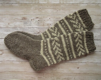 May include: A pair of hand-knitted wool socks. The socks are primarily brown with a cream-colored geometric pattern on the upper portion. The socks are lying on a light-colored wooden surface.