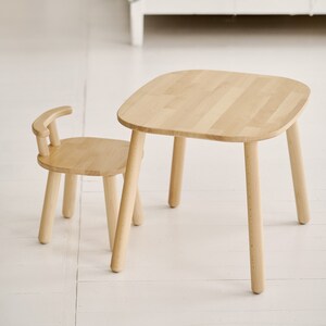 K&ouml;nnte beinhalten: Ein kleines, helles Tisch- und Stuhlset aus Holz. Der Tisch hat eine abgerundete quadratische Oberseite und vier Beine. Der Stuhl hat eine gebogene R&uuml;ckenlehne und vier Beine. Das Set ist aus hellem Holz gefertigt.