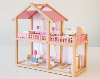 May include: A wooden dollhouse with a pink roof and balcony railings. The two-story house is furnished with miniature furniture, including beds, a sofa, and a bathtub. The interior walls are a light pink color, and the house has white curtains.