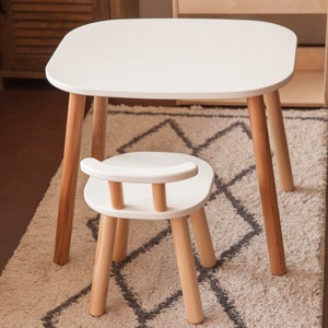 K&ouml;nnte beinhalten: Ein wei&szlig;er Kindertisch mit abgerundeten Ecken und vier Holzbeinen. Ein passender wei&szlig;er Stuhl mit geschwungener R&uuml;ckenlehne und Holzbeinen steht vor dem Tisch. Tisch und Stuhl stehen auf einem gemusterten Teppich.
