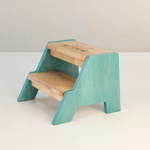 A small, two-tiered wooden step stool with a light blue color.