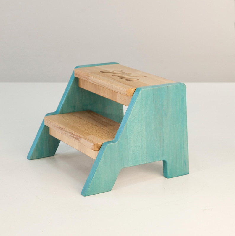 A small, two-tiered wooden step stool with a light blue color.
