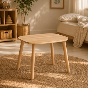 Puede incluir: Una pequeña mesa de madera clara con una parte superior cuadrada y cuatro patas redondeadas. La mesa está sobre una alfombra redonda de yute tejido. La habitación tiene una paleta de colores neutros con luz natural.