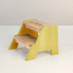 A small, yellow wooden step stool with a simple, minimalist design.