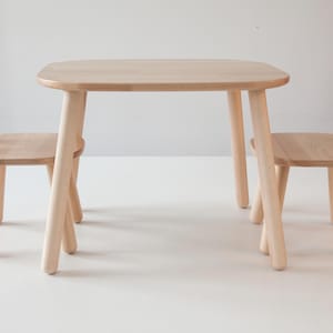 May include: A set of wooden children's furniture, including a table and two chairs. The table and chairs are made of natural wood and have a simple, modern design.