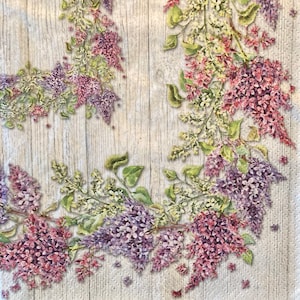 May include: A floral design featuring a wreath of purple and pink flowers with green leaves on a white woodgrain background.