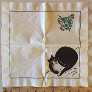 May include: A white paper napkin with a black and white cat illustration and a green and white floral design. The cat is curled up with its tail wrapped around its body. The flowers are in a bouquet and are in the upper right corner of the napkin.